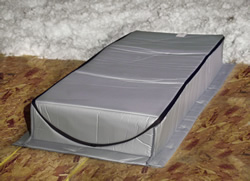 A sizable gray box resting on a warm wooden floor, representing packaging for Attic Tents designed for attic insulation and air sealing solutions.