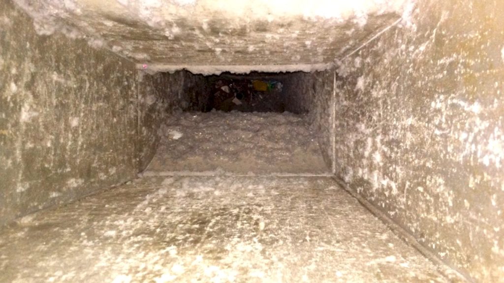 Inside view of a dusty rectangular ventilation duct with visible debris and grime buildup, highlighting the need for professional duct cleaning and maintenance.
